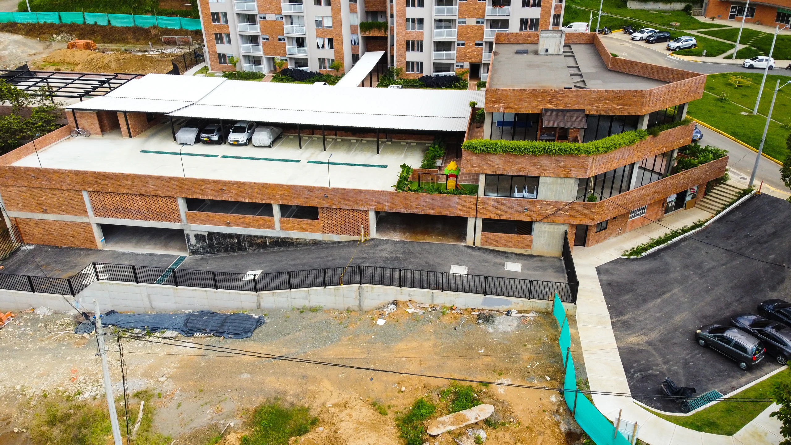 Detalle del zócalo de ladrillo: parqueo semienterrado abajo, cubierta transitable arriba y las terrazas comunes sembradas escalonándose con el terreno.